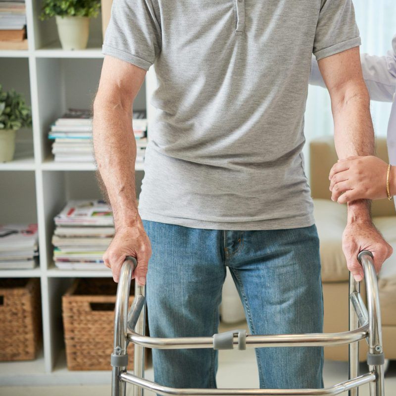 Faceless shot of senior man in disability standing with metal walker and trying to walk with help of doctor